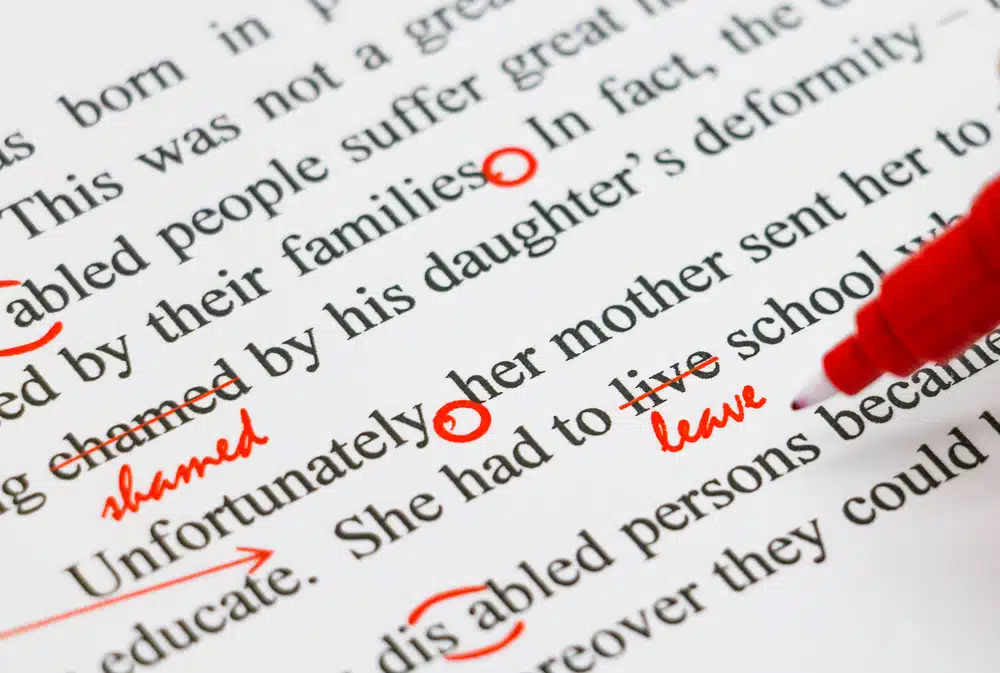 Close-up of a proofread English document with red pen marks highlighting corrections, crossed-out words, and inserted text, symbolizing error detection and text comparison.